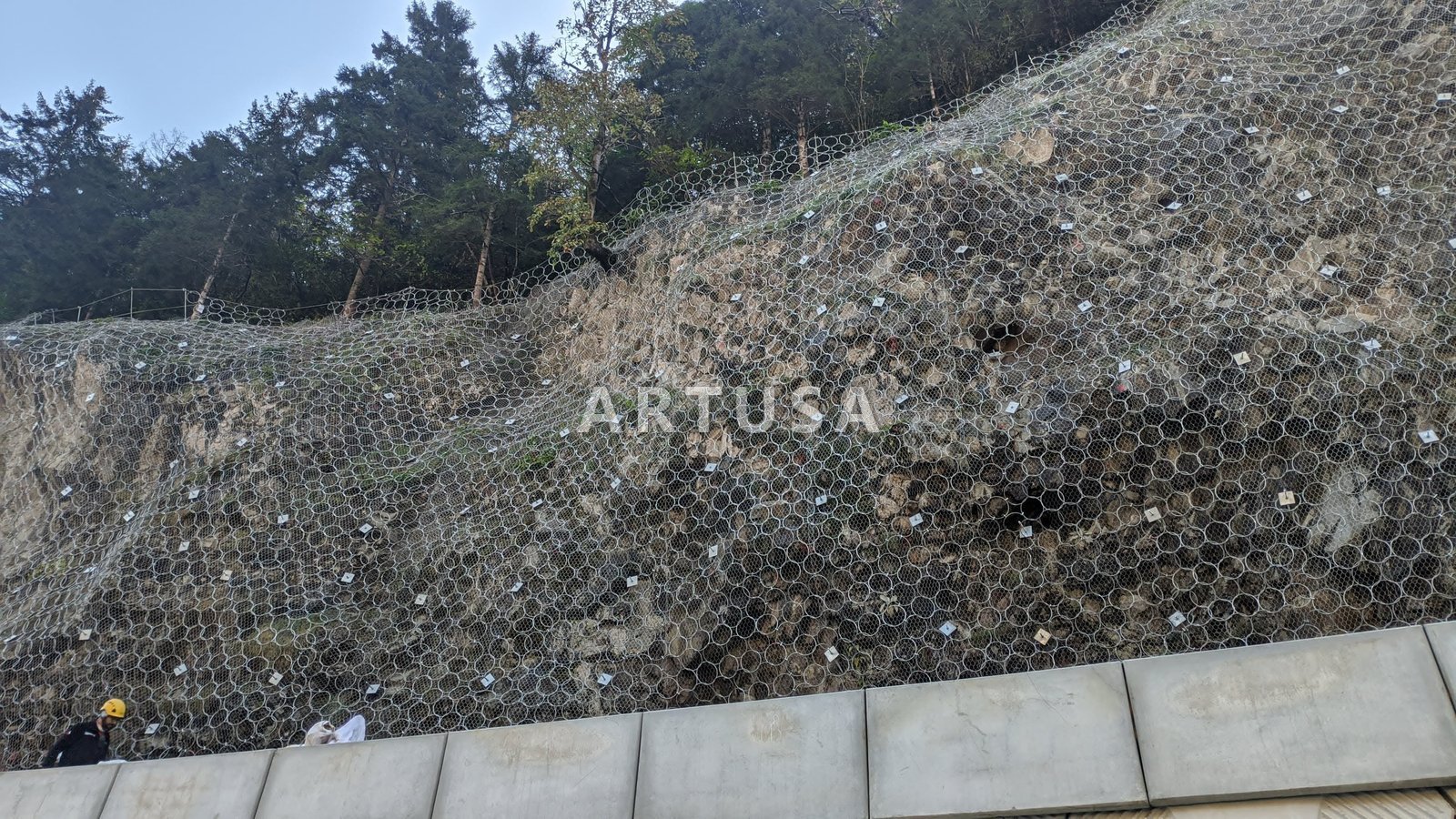 Mesh on a rock face above a retaining wall